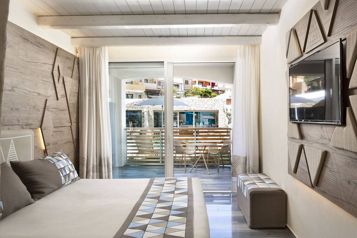 Un dormitorio moderno con una cama grande, vista al balcón y un comedor con sillas.