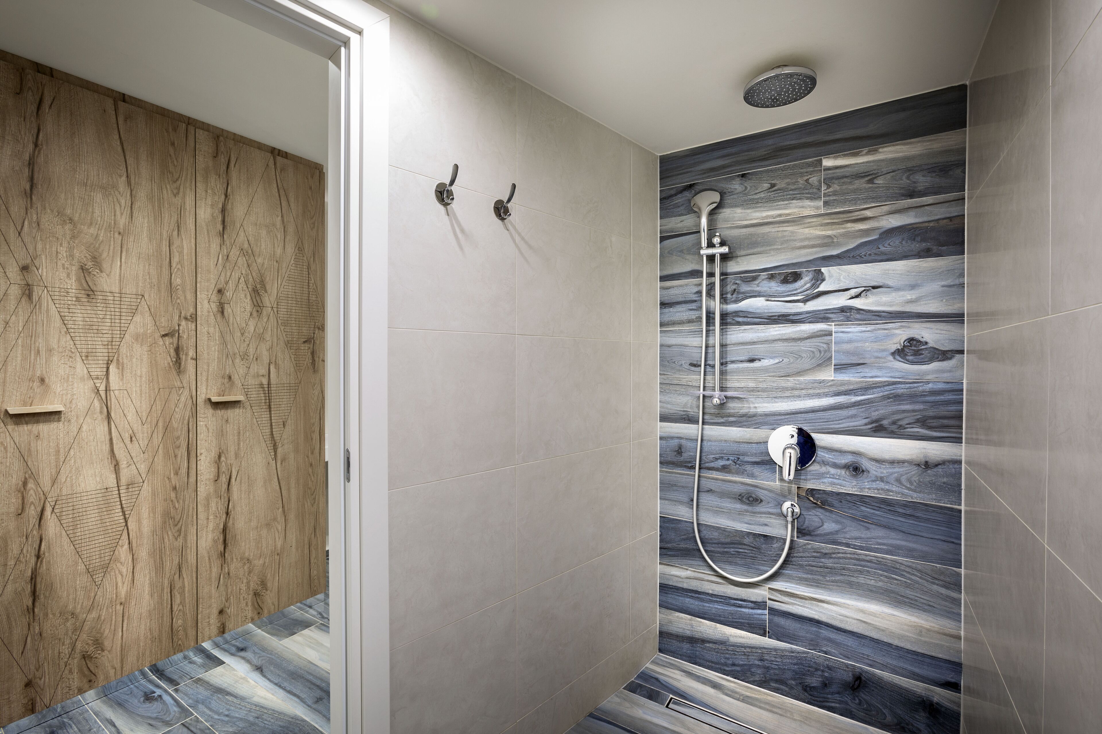Un baño moderno con tocador de madera, ducha con cabezal de lluvia y pared con estampado de mármol.