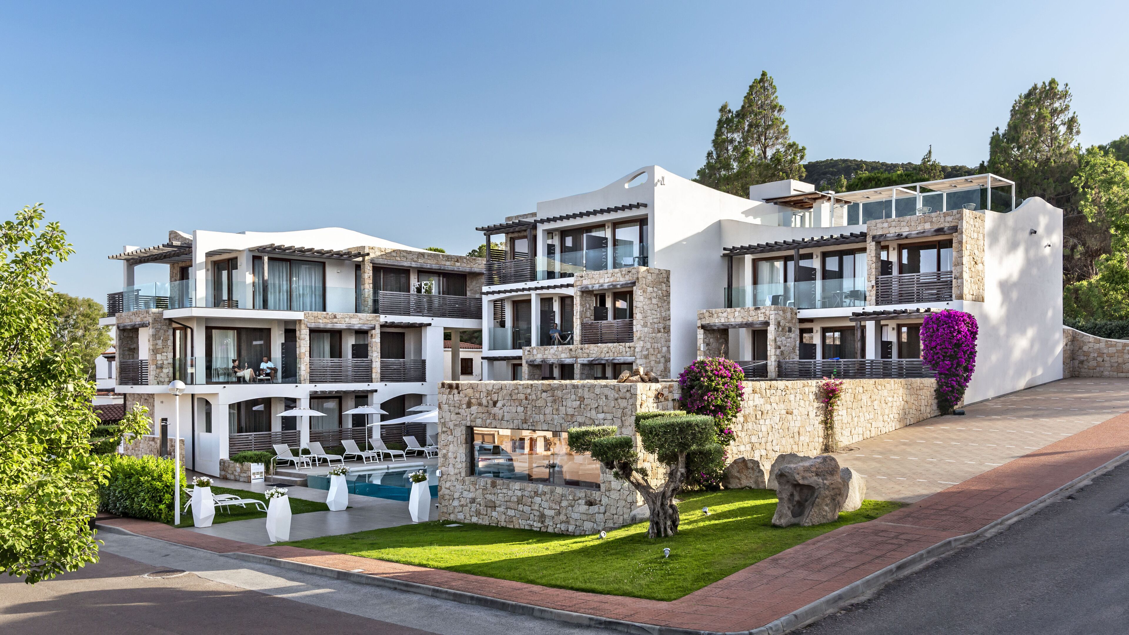 A modern multi-story hotel with balconies, a swimming pool, and a landscaped garden.