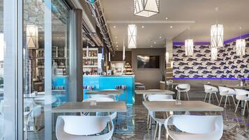 Un restaurante moderno con barra, sillas blancas y un muro estampado.