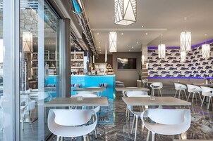 Un restaurante moderno con barra, sillas blancas y un muro estampado.