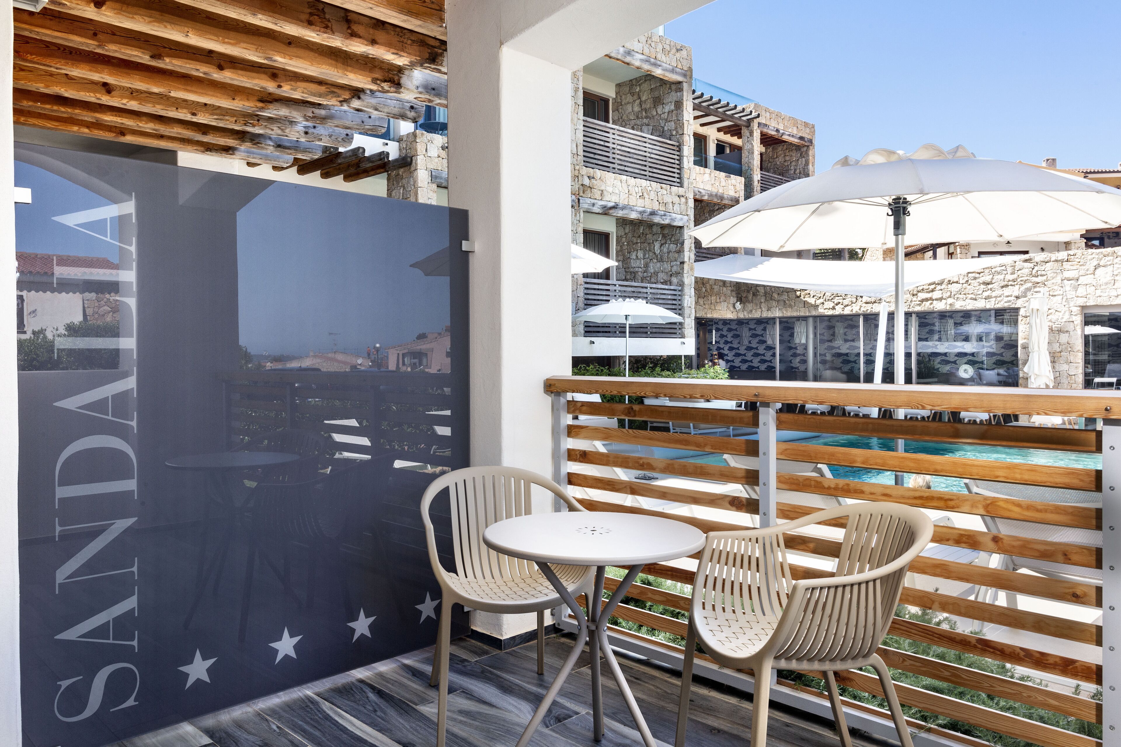 A balcony with a view of a pool, two white chairs, and a table.