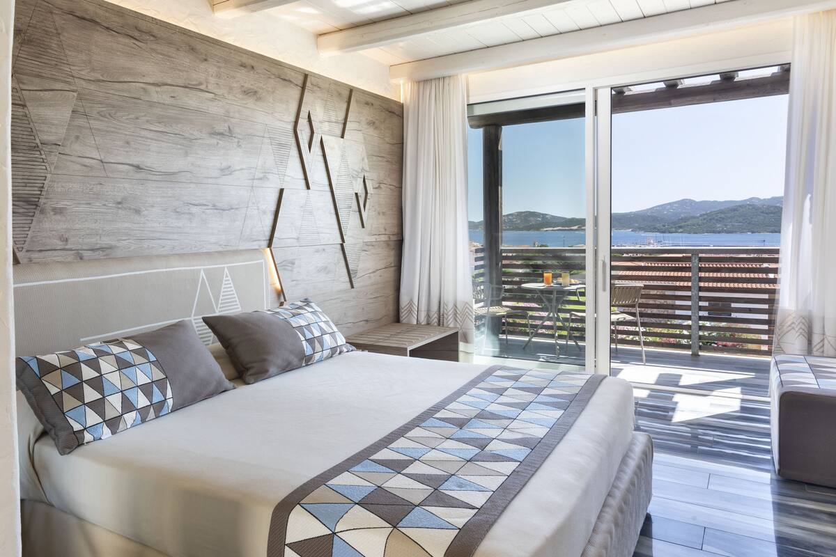 Un dormitorio moderno con una cama grande, un cabecero de madera y un balcón con vista al mar.