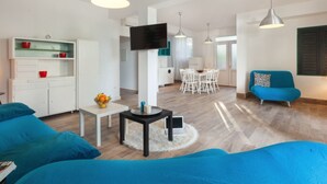 A modern living room with a sofa, a coffee table, and a TV. There is a dining area with a table and chairs. - Villa Zorana (Brela)
