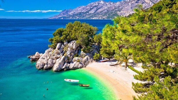 A beach with clear turquoise waters, a rocky outcrop, and a boat anchored near the shore. - Villa Zorana (Brela)