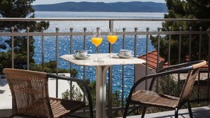 A balcony with a table and two wicker chairs, overlooking a body of water and distant hills. - Villa Zorana (Brela)