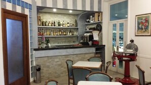 A bar area with shelves of liquor bottles, a coffee machine, and a vintage espresso machine. There are tables and chairs for seating. - Hotel San Giorgio (Alassio)