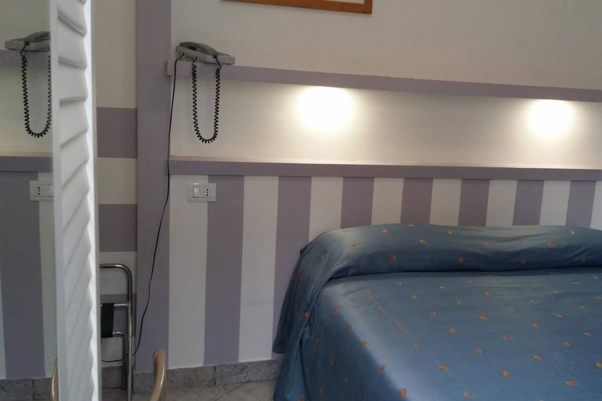 A bedroom with a striped headboard, a bed with a blue bedspread, and a telephone on the wall.