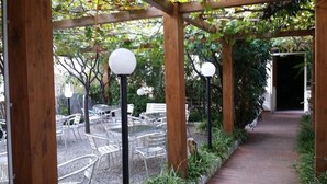 An outdoor patio area with tables and chairs, wooden pergola structures, and a brick pathway. - Hotel San Giorgio (Alassio)