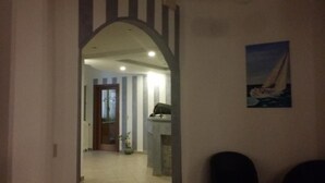 A hallway with a view into a room featuring a fireplace, a potted plant, and a painting of a sailboat. - Hotel San Giorgio (Alassio)