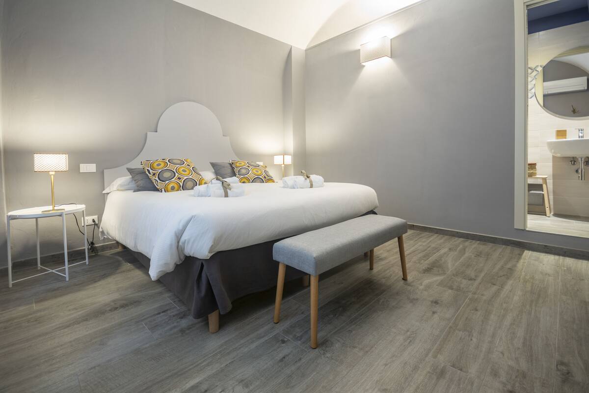 A modern bedroom with a large bed, bedside tables, a bench, and a mirror.