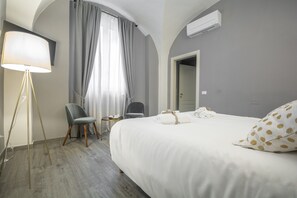 A hotel room with a large bed, a desk, a chair, a lamp, and a window with curtains. - La Lu Cozy Rooms (Pisa)
