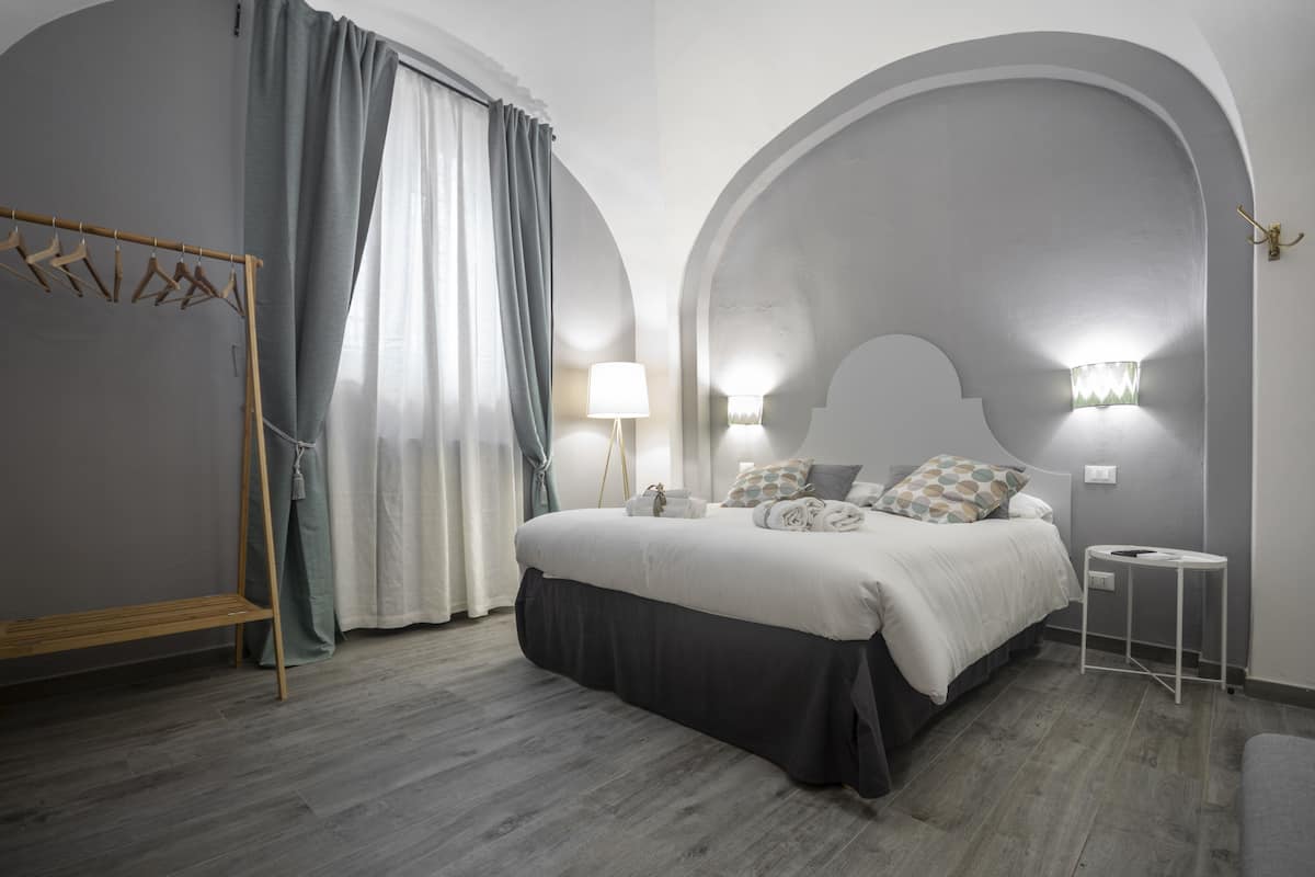 A bedroom with a bed, a bedside table, a lamp, a wardrobe, and a hanging rack.