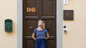 Una mujer está de pie frente a una puerta marrón con un letrero que dice "B&B" y el número "2" en la pared a su lado.