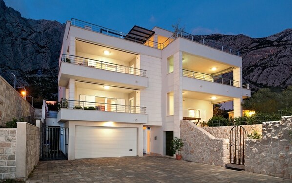A modern multi-story building with balconies, a garage, and a stone retaining wall.