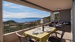 A balcony with a table set for dining, overlooking a scenic view of the sea and hills.
