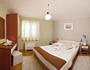 A neatly arranged bedroom with a bed, bedside tables, a wardrobe, a window with curtains, and a hanging light fixture.