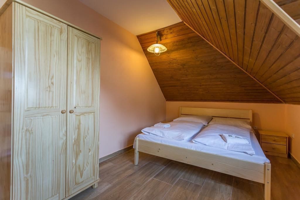 A bedroom with a wooden wardrobe, a bed with white bedding, and a sloped ceiling.