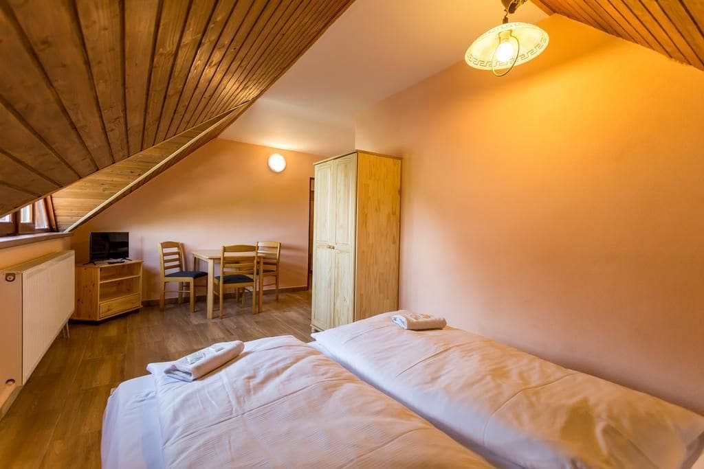 Une chambre avec deux lits, une armoire en bois, un bureau avec une chaise et un téléviseur posé sur un meuble.