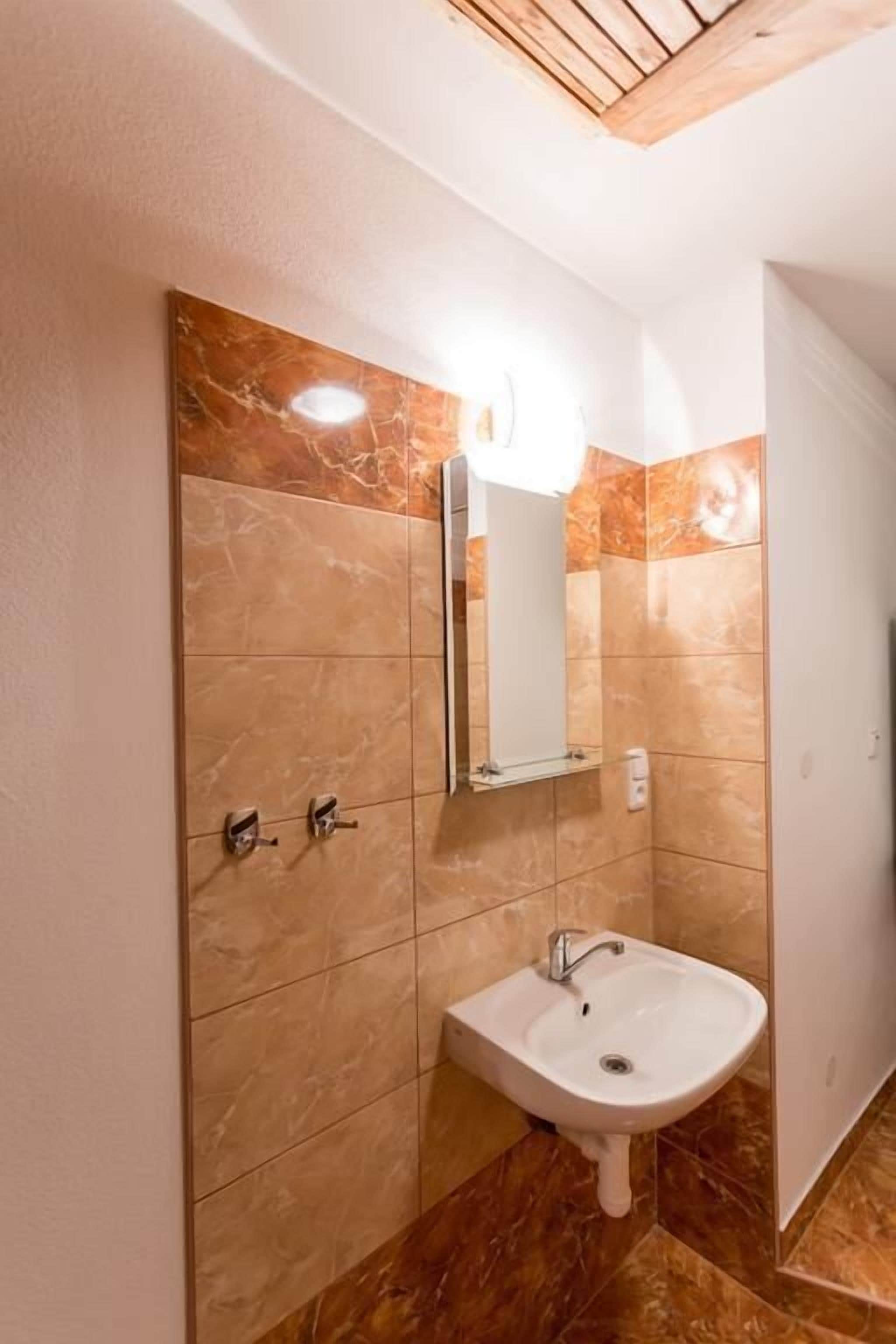Un baño con pared de azulejos de mármol, un lavabo blanco y un espejo.