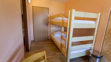 Habitación con literas, una puerta de madera, un cubo de basura y una silla de madera.