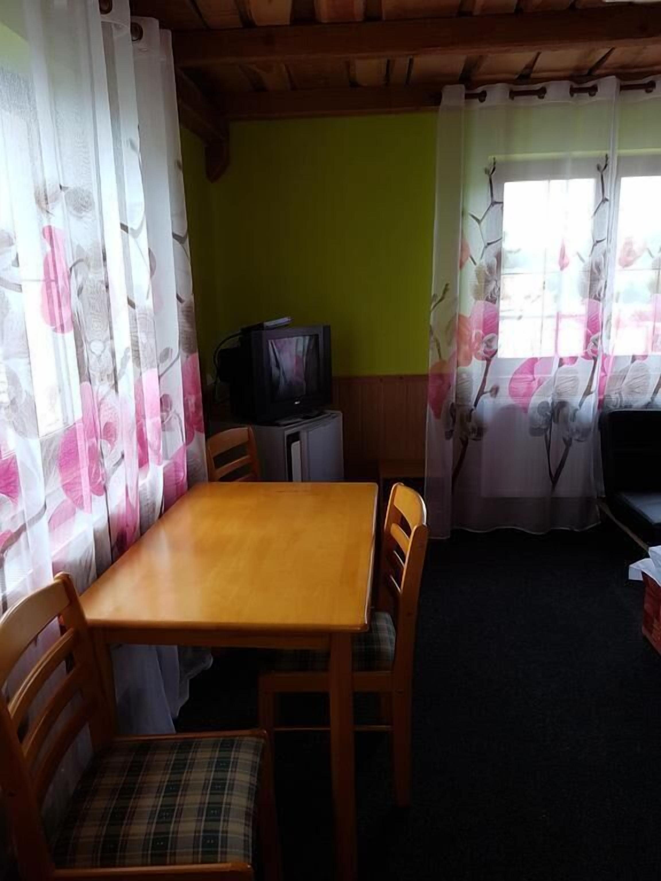 A small, cozy room with a wooden table and chairs, a television, and curtains with floral patterns.