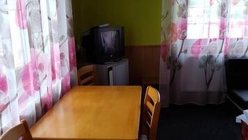 A small, cozy room with a wooden table and chairs, a television, and curtains with floral patterns.