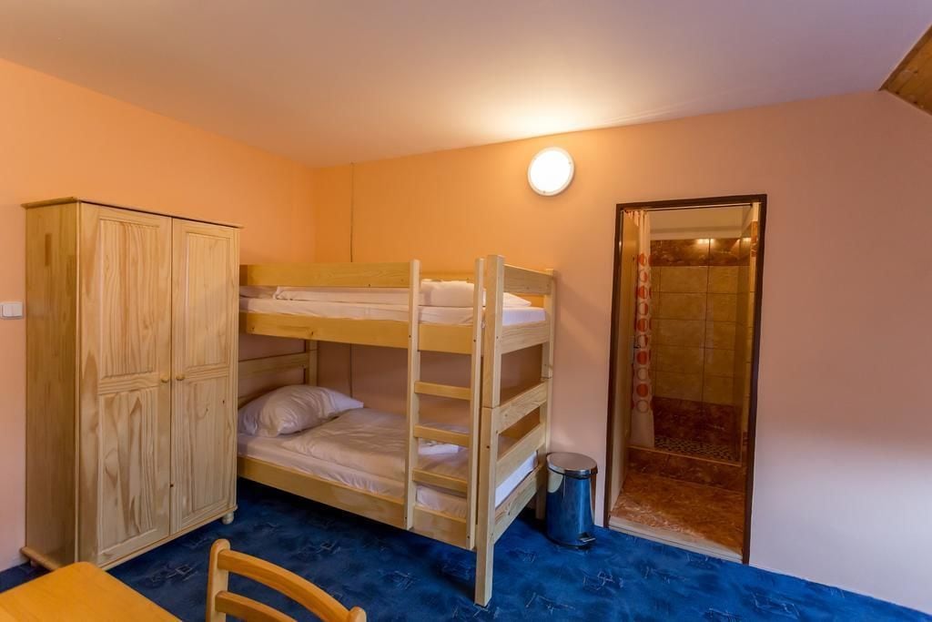 A bunk bed room with a wooden wardrobe, a small table, and a trash bin.