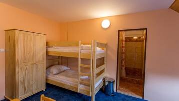 A bunk bed room with a wooden wardrobe, a small table, and a trash bin.