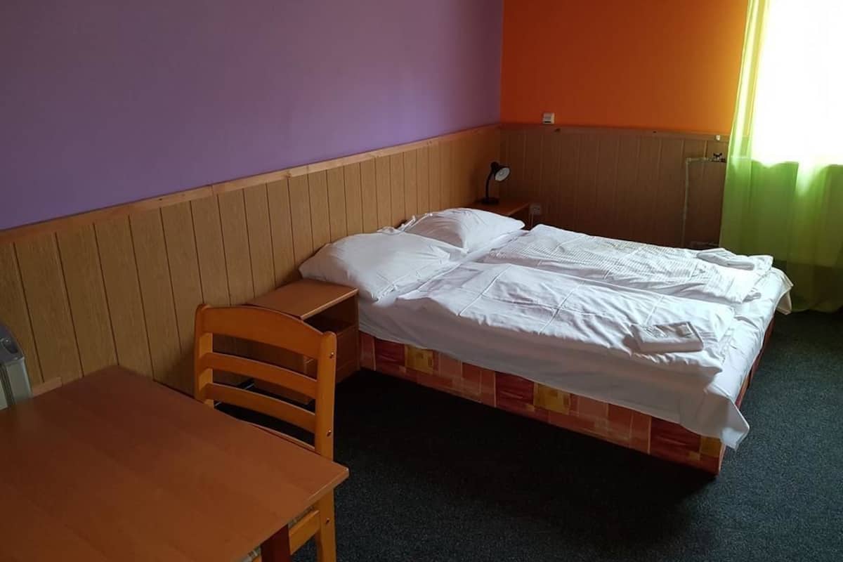 Une petite chambre avec un lit simple, une tête de lit en bois, une table en bois et une lampe de chevet.