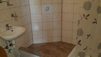 Un bany amb plat de dutxa cantonadat, un rentapeus i un vàter.