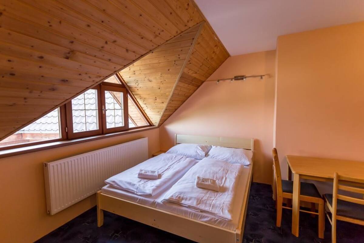 Une chambre avec un plafond en pente, un lit recouvert de draps blancs, une table en bois et une chaise.