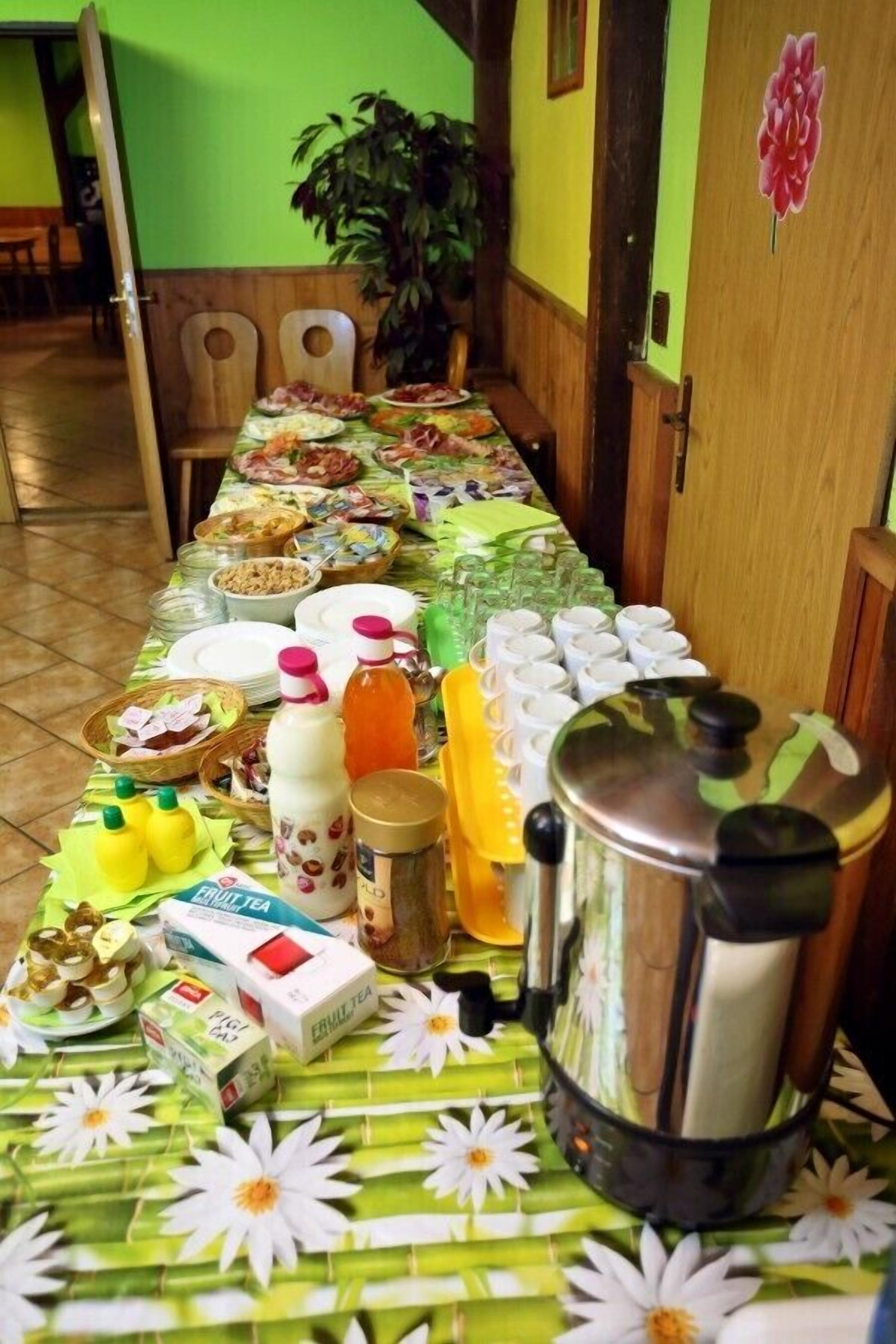 A dining table set with various food items and beverages, a coffee maker, and a plant in the background.
