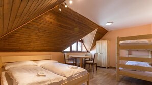 Un dormitorio con techo de madera inclinado, una litera, un escritorio con sillas y un radiador.