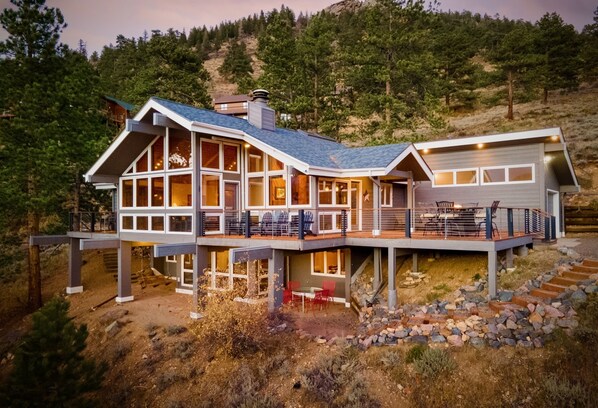 A modern multi-story house with large windows, a deck, and a staircase leading to the upper level.