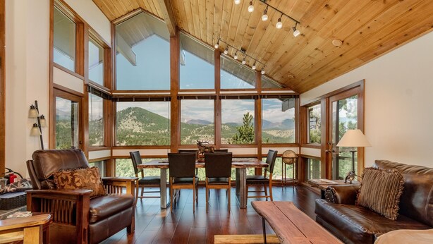 A spacious room with a high ceiling, large windows offering a mountain view, wooden furniture, and a dining area. - Herondale Luxury Vacation  At Windcliff 3 Bedroom Home by RedAwning (Estes Park)