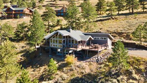 A modern two-story house with a large deck and multiple windows, surrounded by a mountainous landscape with pine trees. - Herondale Luxury Vacation  At Windcliff 3 Bedroom Home by RedAwning (Estes Park)