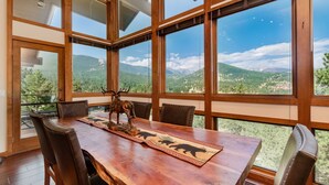 A dining area with a wooden table, leather chairs, and a scenic mountain view through large windows. - Herondale Luxury Vacation  At Windcliff 3 Bedroom Home by RedAwning (Estes Park)