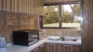 Una cocina con armarios de madera, microondas, hervidor, lavabo y ventana con vista a árboles.
