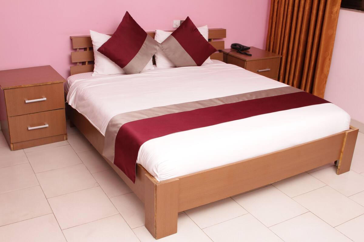 A neatly made bed with a wooden frame and a white mattress, flanked by two nightstands with drawers, one of which has a telephone.