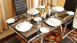 Mesa de comedor preparada para cuatro personas, con una botella de vino, copas y cubiertos.