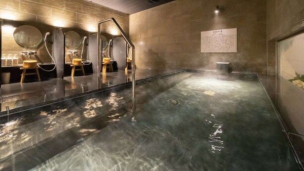 A modern spa with a large heated pool, wooden benches, and a wall-mounted mirror. - Super Hotel Yamaguchi Yuda Onsen (Yamaguchi)