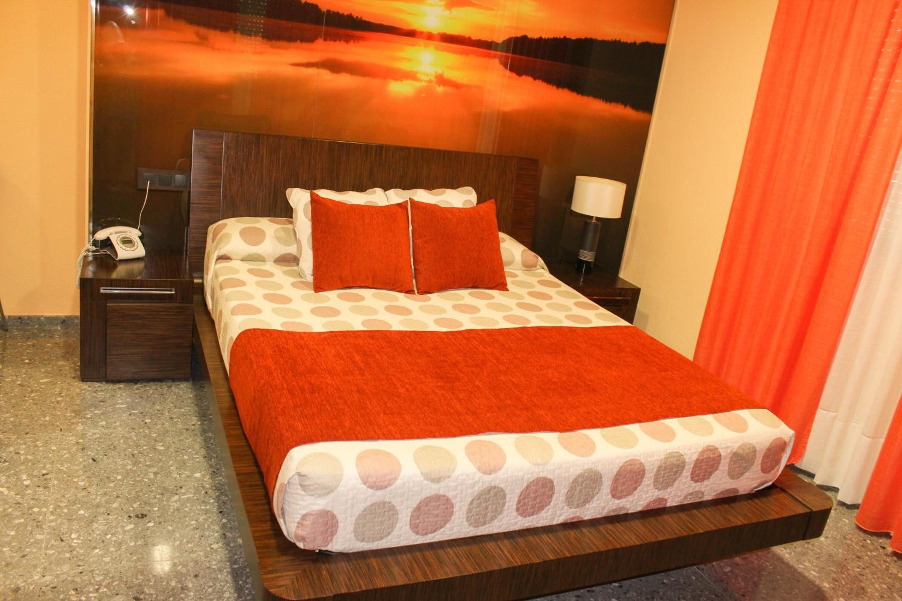 Una habitación de hotel con una cama, una mesita de noche, una lámpara y vistas a un atardecer sobre el agua.