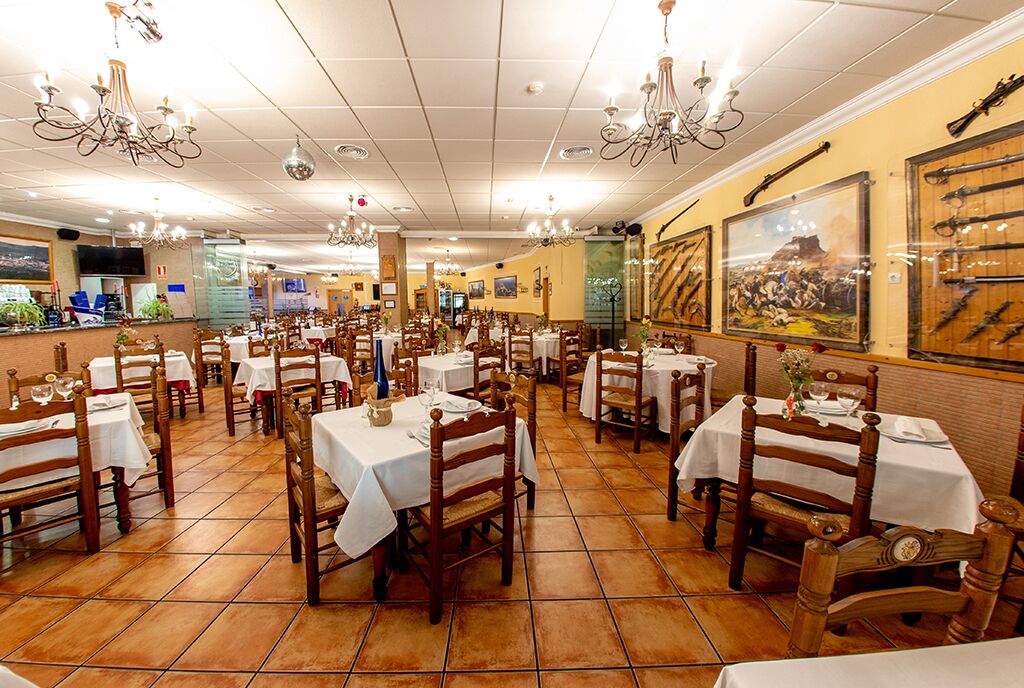 Un restaurante con varias mesas y sillas, piso de baldosas y lámparas de araña.