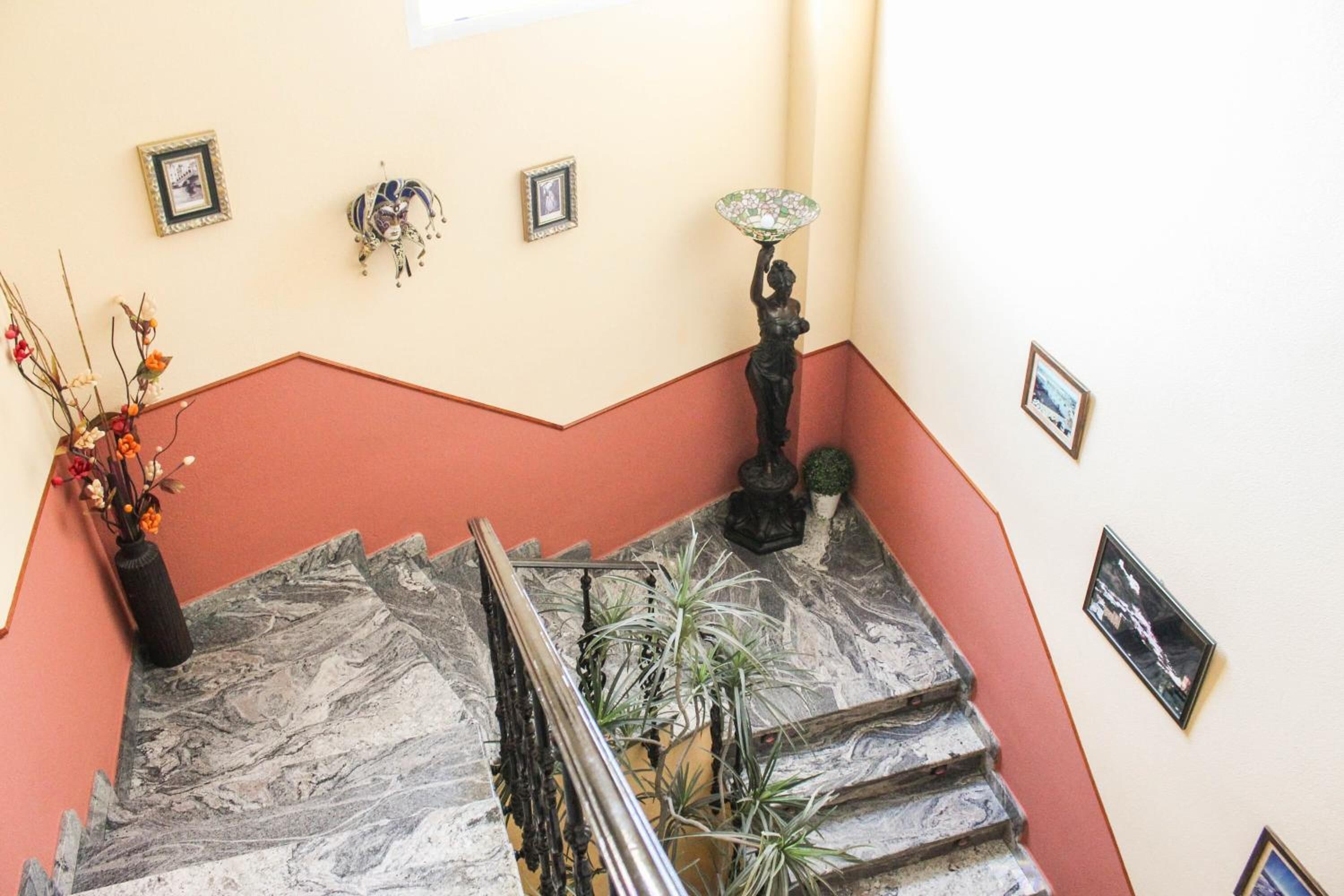 A marble staircase with a red accent wall, a vase with flowers, and a statue holding a fan.