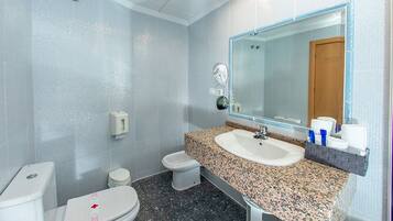 A bathroom with a white toilet, a bidet, a sink with a granite countertop, and a mirror above the sink.