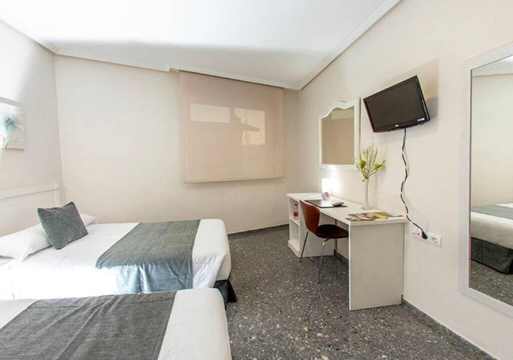 Habitación de hotel con dos camas, un escritorio, una silla, un televisor y una ventana con persianas.