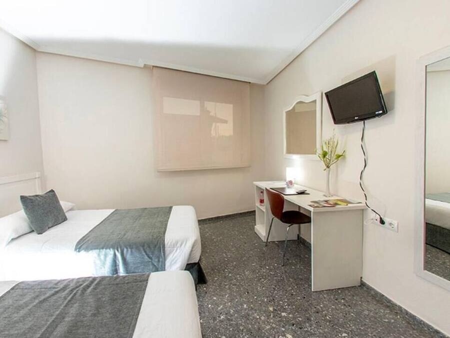 Habitación de hotel con dos camas, un escritorio, una silla, un televisor y una ventana con persianas.
