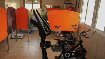A gym with exercise equipment, orange partitions, and a window with natural light.