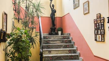 Eine Marmortreppe mit roten Akzenten, umgeben von Topfpflanzen und gerahmten Bildern an den Wänden.